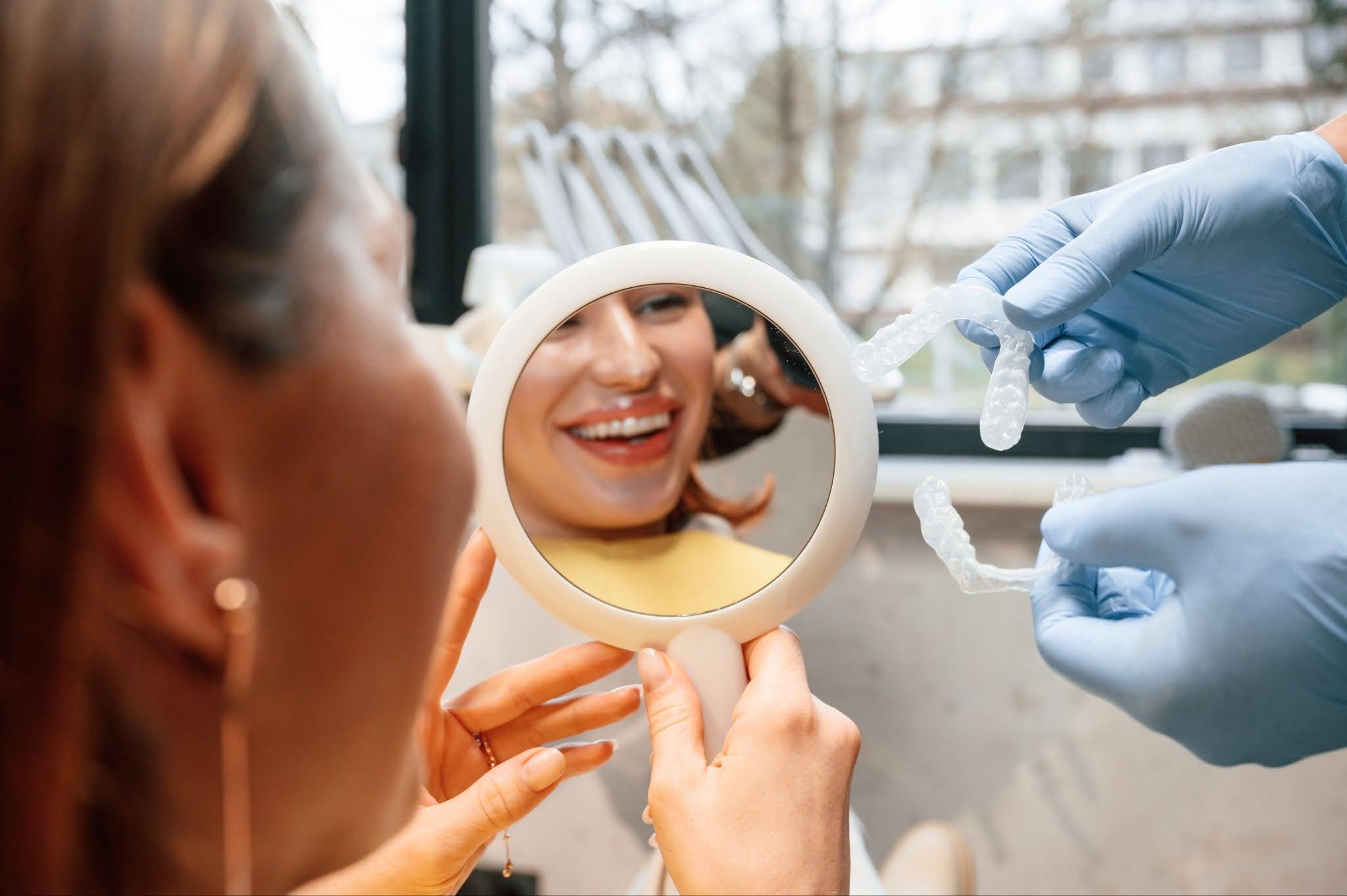 Patient smiling at her reflection in a dental mirror while a dentist holds a custom porcelain restoration at Spicewood Dental in Austin, TX